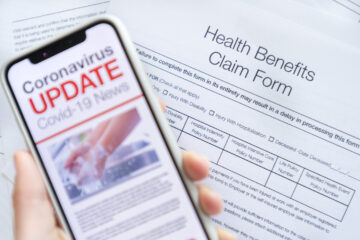 Close up of a mobile phone with Coronavirus covid-19 news update. There is a health benefits claim form in the background. The phone is being held and has an image of hand washing hygiene.